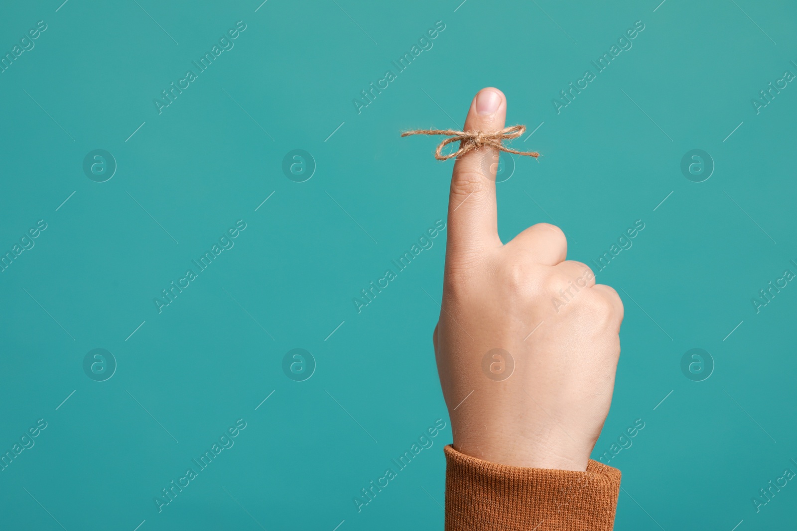 Photo of Man showing index finger with tied bow as reminder on turquoise background, closeup. Space for text