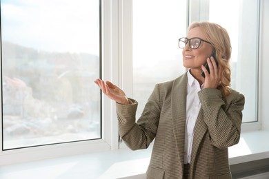 Photo of Lady boss talking on smartphone near window indoors, space for text. Successful businesswoman