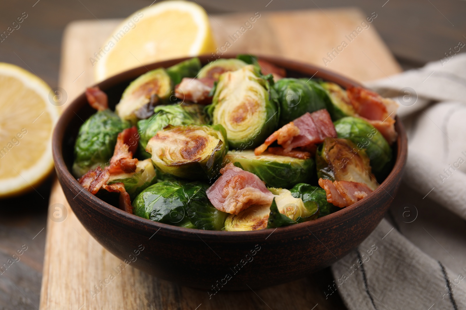 Photo of Delicious roasted Brussels sprouts and bacon in bowl on table, closeup