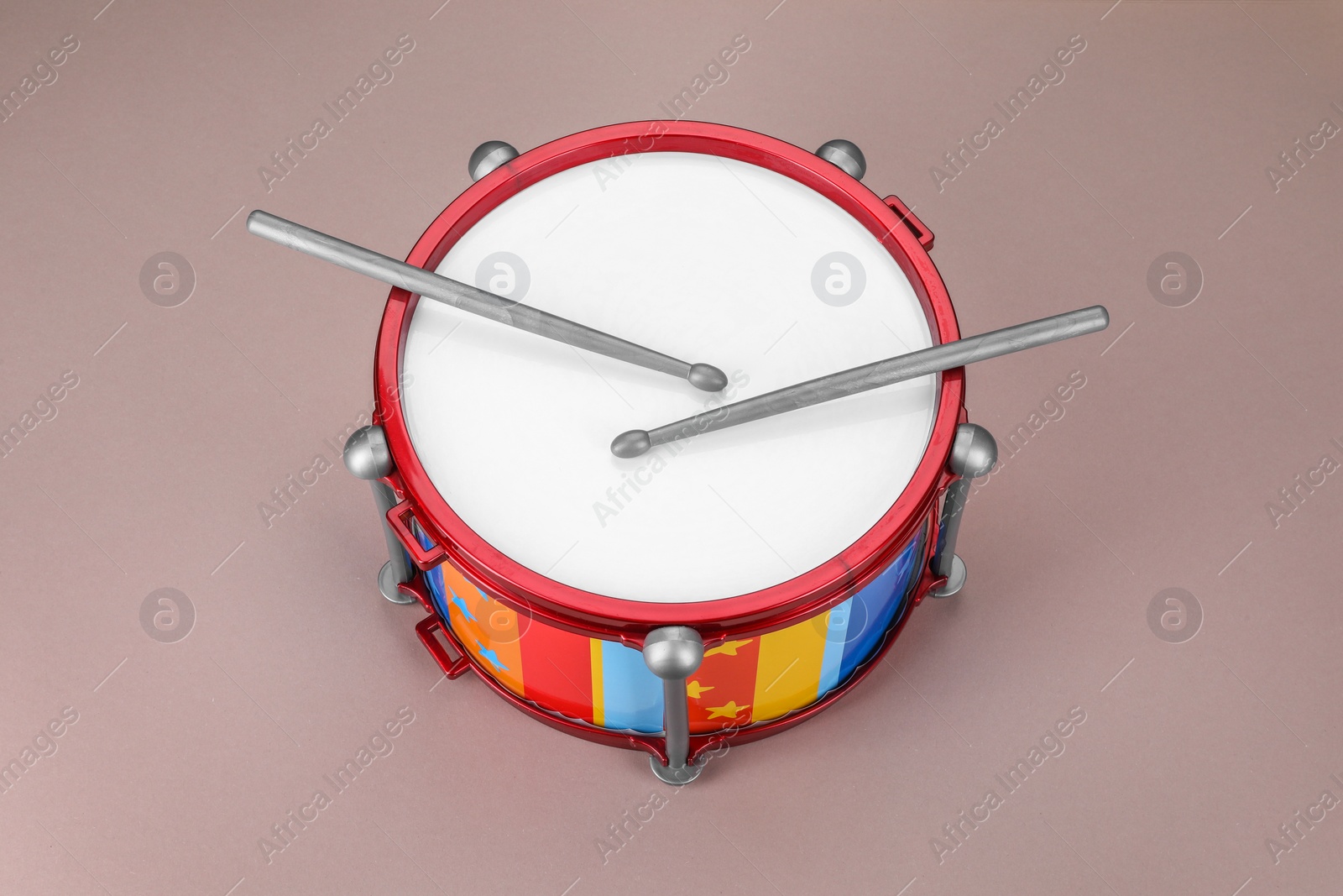 Photo of Colorful drum and sticks on dusty rose background. Percussion musical instrument