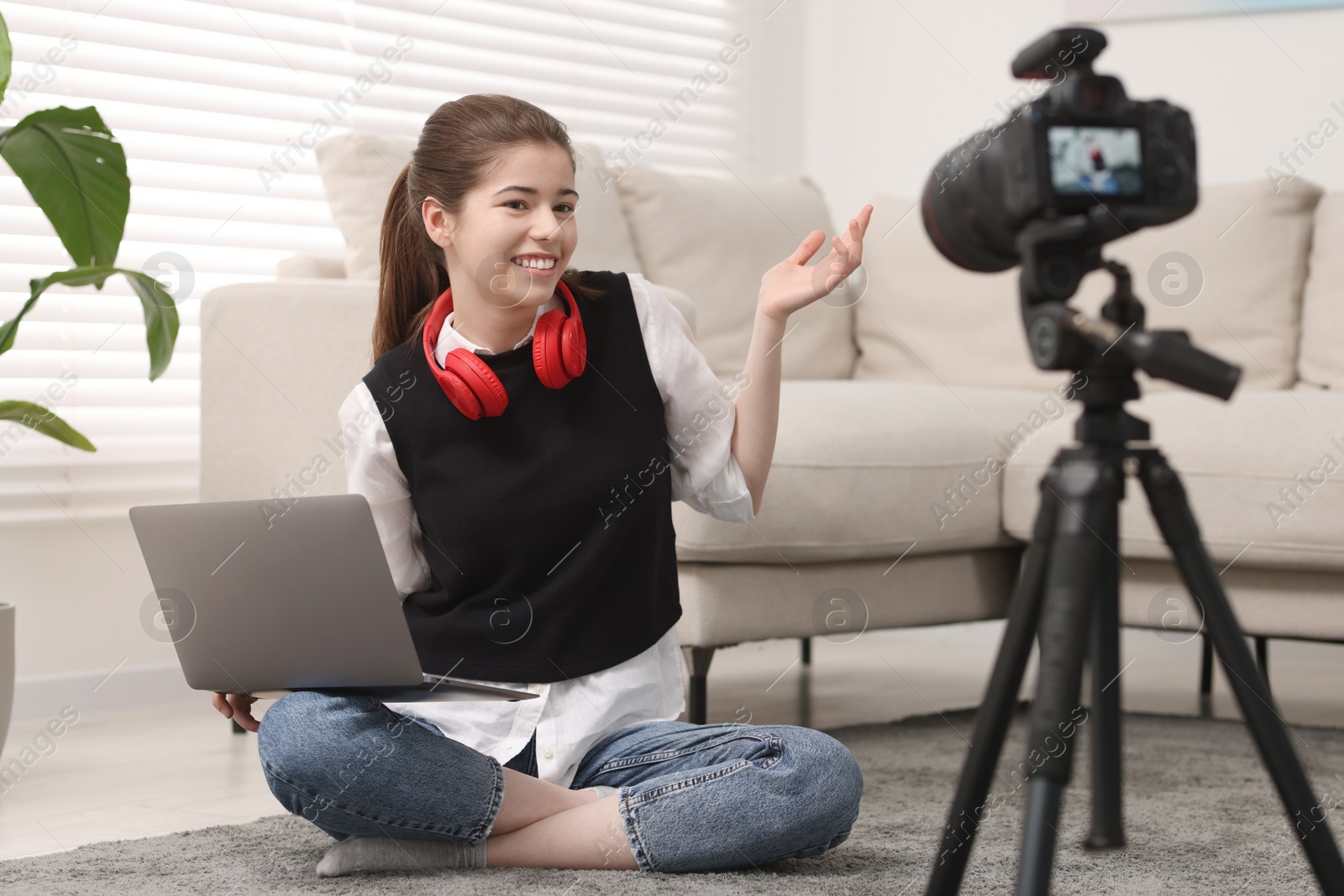 Photo of Smiling teenage blogger with laptop explaining something while streaming at home