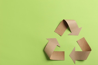 Photo of Recycling symbol cut out of kraft paper on green background, top view. Space for text