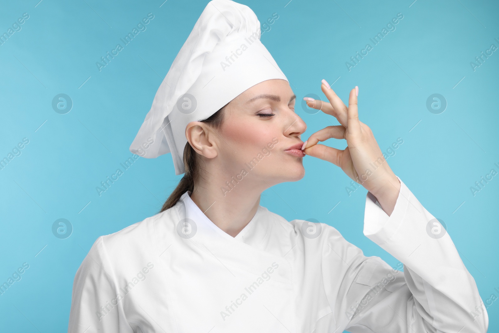 Photo of Woman chef in uniform showing perfect sign on light blue background