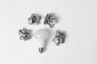 Photo of Composition with lamp bulb and crumpled banknotes on white background, top view. Creative concept