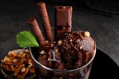 Photo of Tasty chocolate ice cream with sauce, nuts and wafer rolls in glass dessert bowl on table, closeup