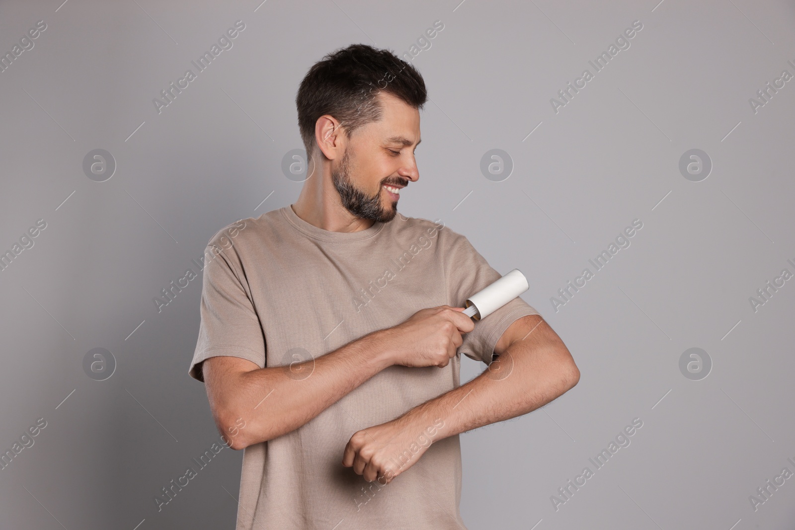 Photo of Handsome man using lint roller on light grey background