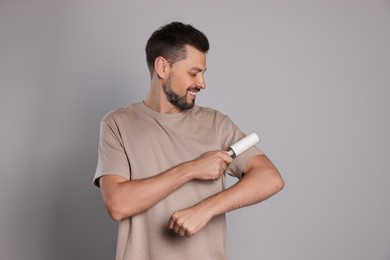 Handsome man using lint roller on light grey background