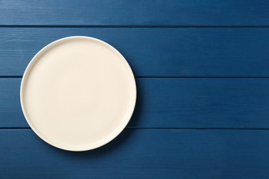 Photo of Clean white plate on wooden blue table, top view. Space for text