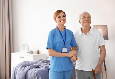Photo of Nurse in uniform assisting elderly woman indoors. Space for text