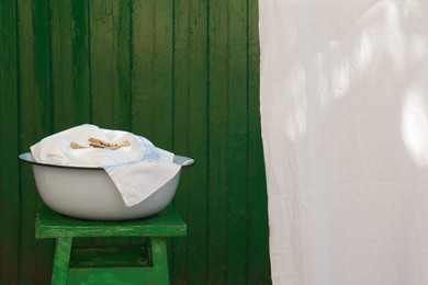 Basin with clean laundry and pile of clothespins outdoors