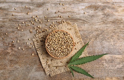 Bowl of hemp seeds on wooden background, top view