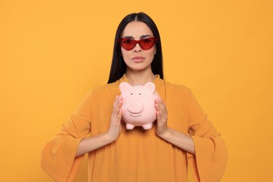Photo of Sad young woman with piggy bank on orange background