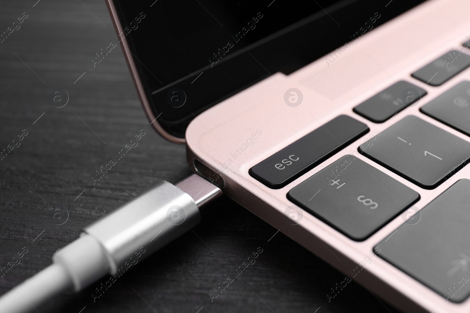 Photo of USB cable with type C connector and laptop on black wooden table, closeup