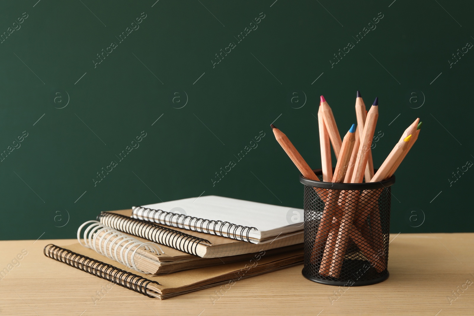 Photo of Different school stationery on wooden table near green chalkboard. Back to school