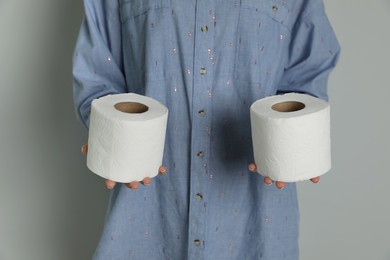 Woman with toilet paper rolls on grey background, closeup