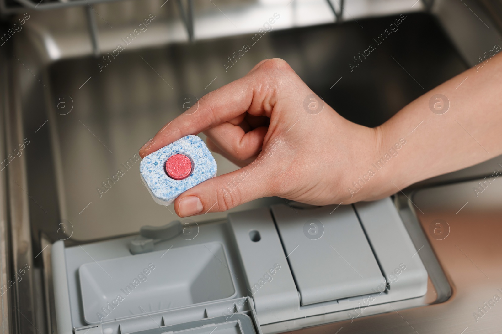 Photo of Woman putting detergent tablet into open dishwasher, closeup