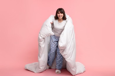 Happy woman in pyjama wrapped in blanket on pink background