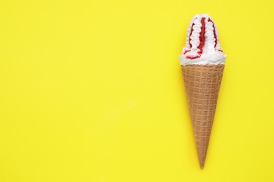Photo of Delicious ice cream with raspberry jam in waffle cone on yellow background, top view. Space for text