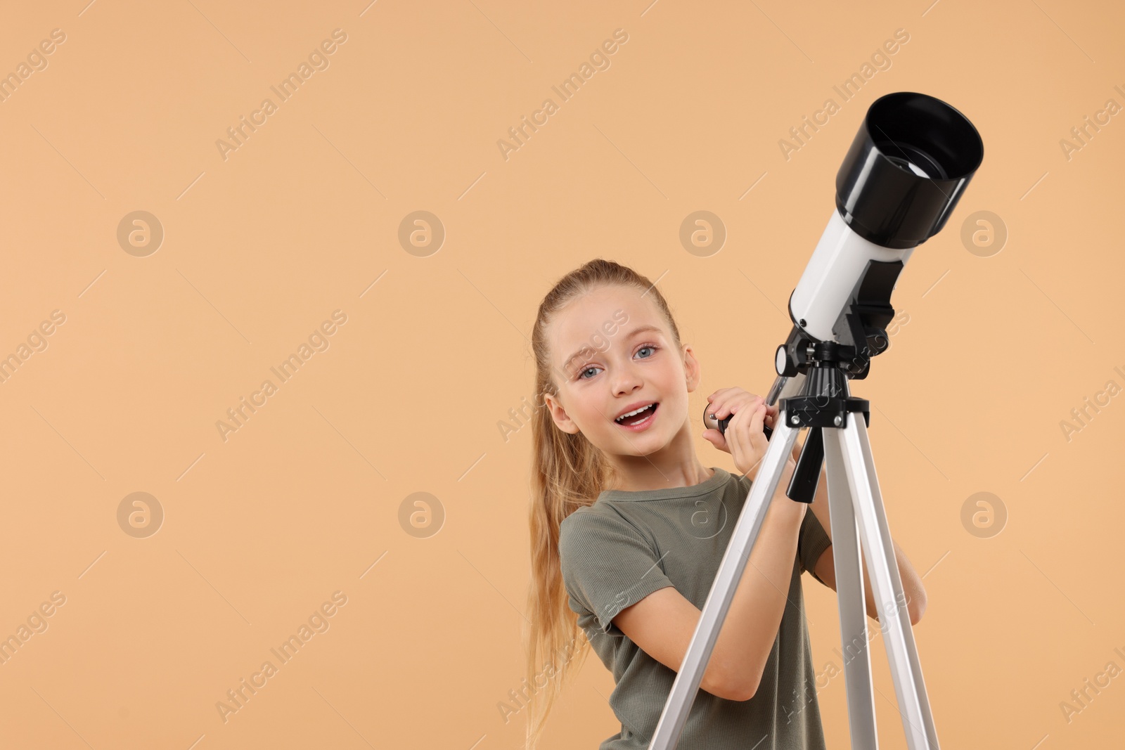 Photo of Happy little girl with telescope on beige background, space for text