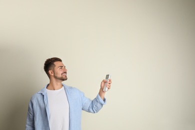 Photo of Happy young man operating air conditioner with remote control on beige background. Space for text