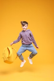 Photo of Back to school. Cute boy with backpack jumping on orange background