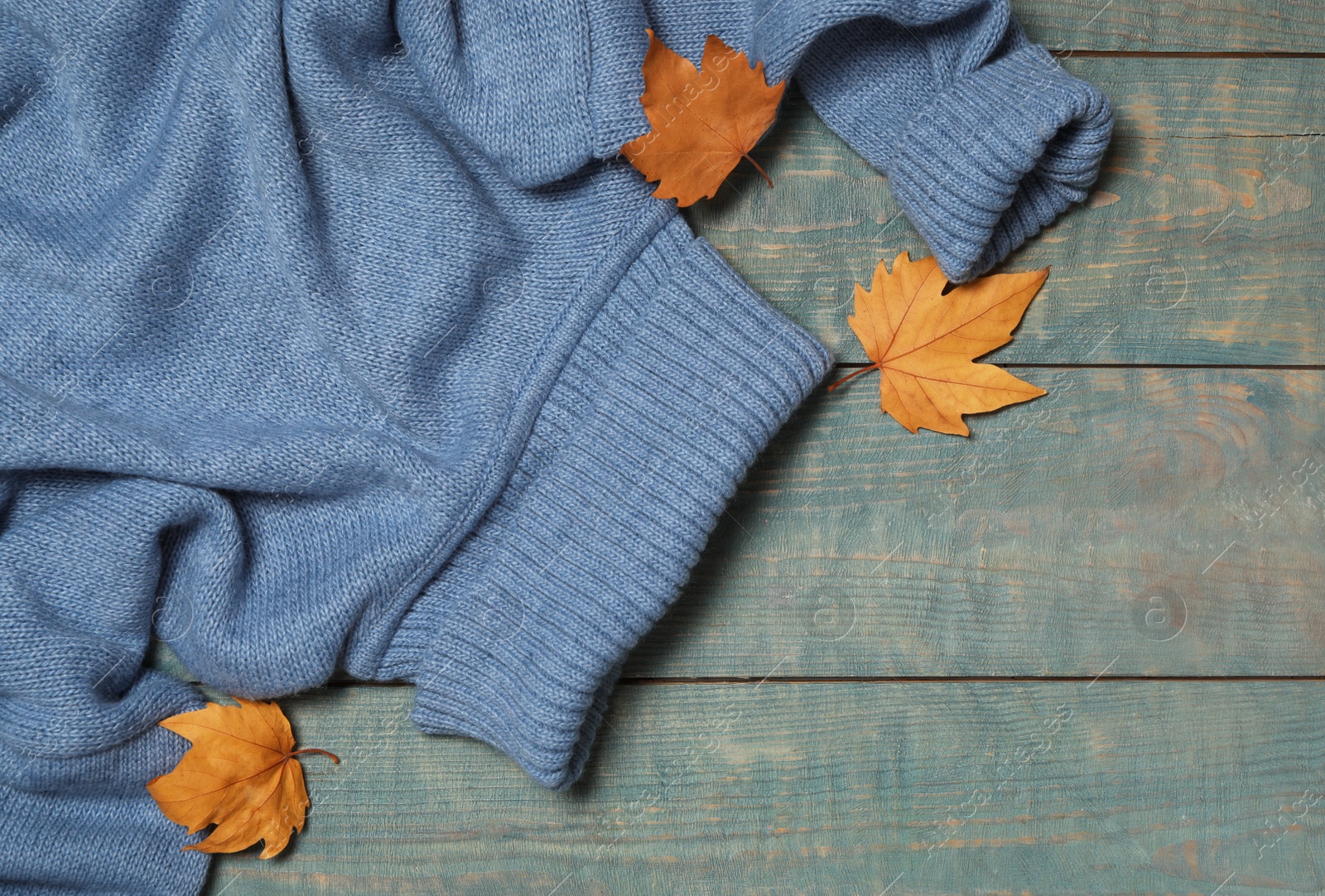 Photo of Warm sweater and dry leaves on blue wooden background, flat lay. Autumn season