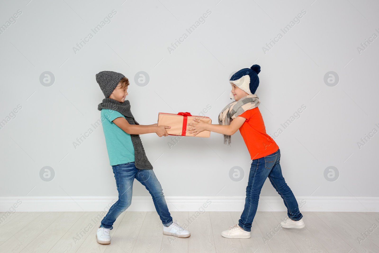 Photo of Cute little children in warm clothes with Christmas gift box on light wall background