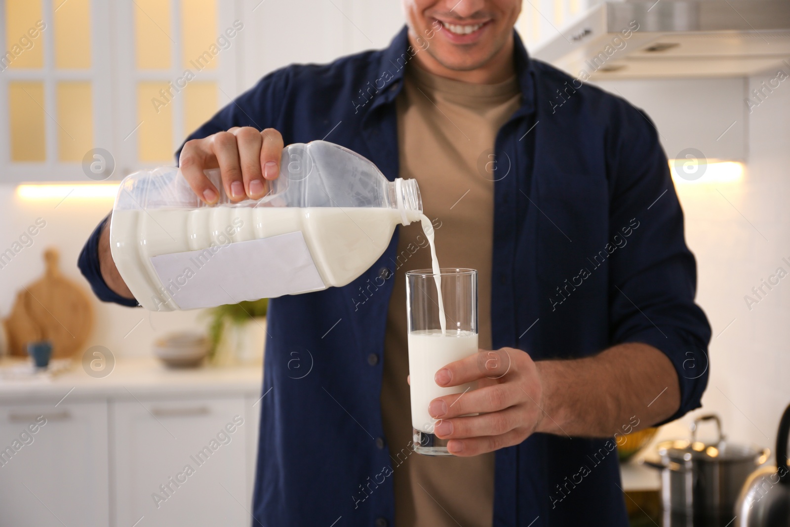 Photo of Man pouring milk from gallon bottle into glass in kitchen, closeup
