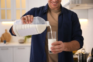 Man pouring milk from gallon bottle into glass in kitchen, closeup