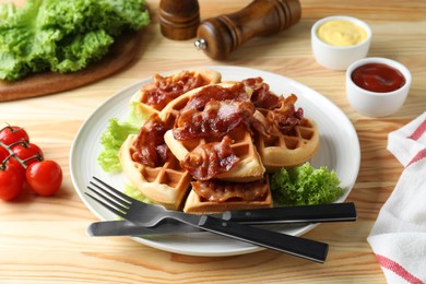 Tasty Belgian waffles served with bacon, lettuce and sauces on wooden table