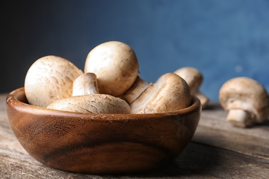 Bowl of fresh champignon mushrooms on table against color background, closeup