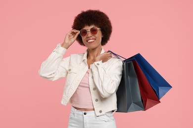 Photo of Happy young woman in stylish sunglasses with shopping bags on pink background