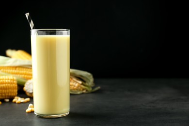 Photo of Freshly made corn juice in glass on grey table against black background. Space for text
