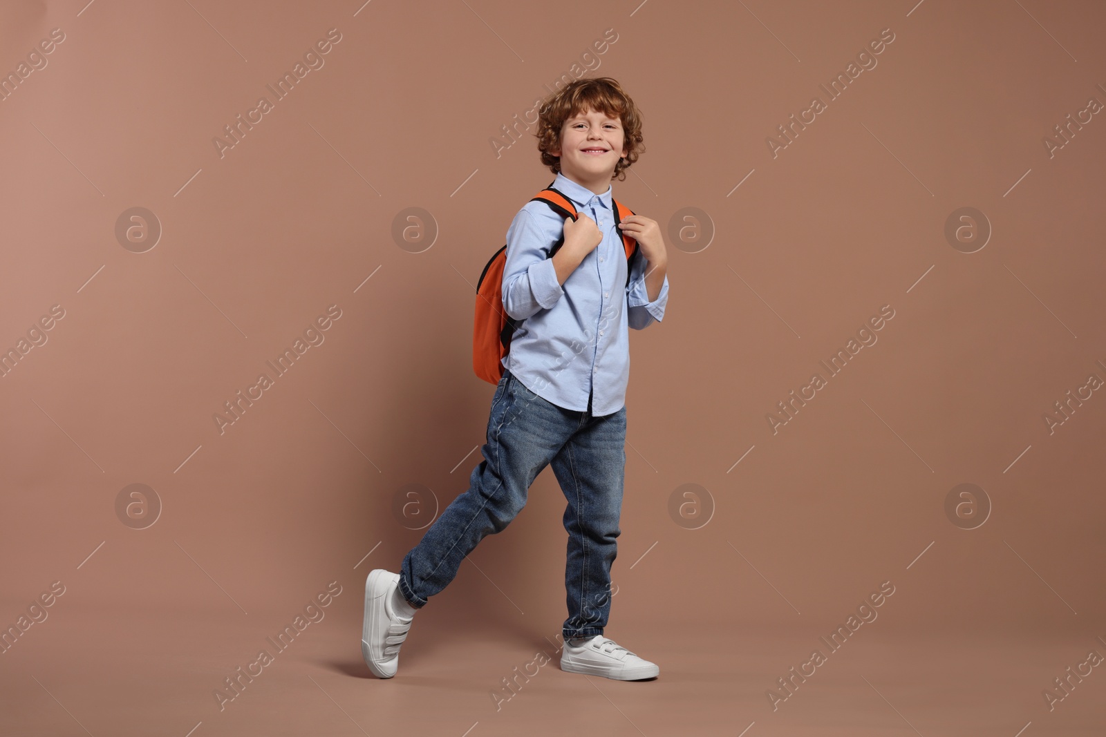 Photo of Happy schoolboy with backpack on brown background