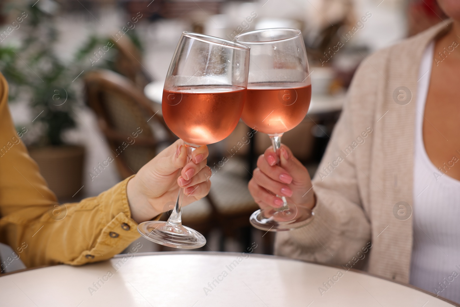Photo of Women clinking glasses with rose wine at white table in outdoor cafe, closeup