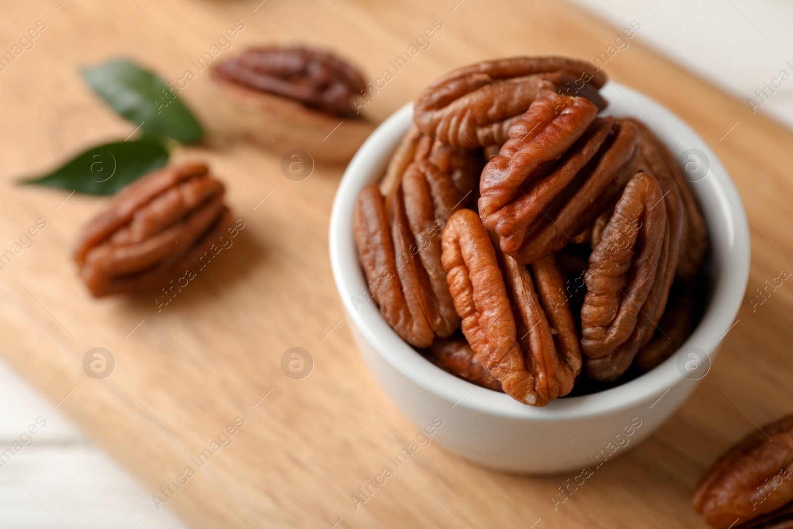 Photo of Shelled pecan nuts in bowl on wooden board. Space for text