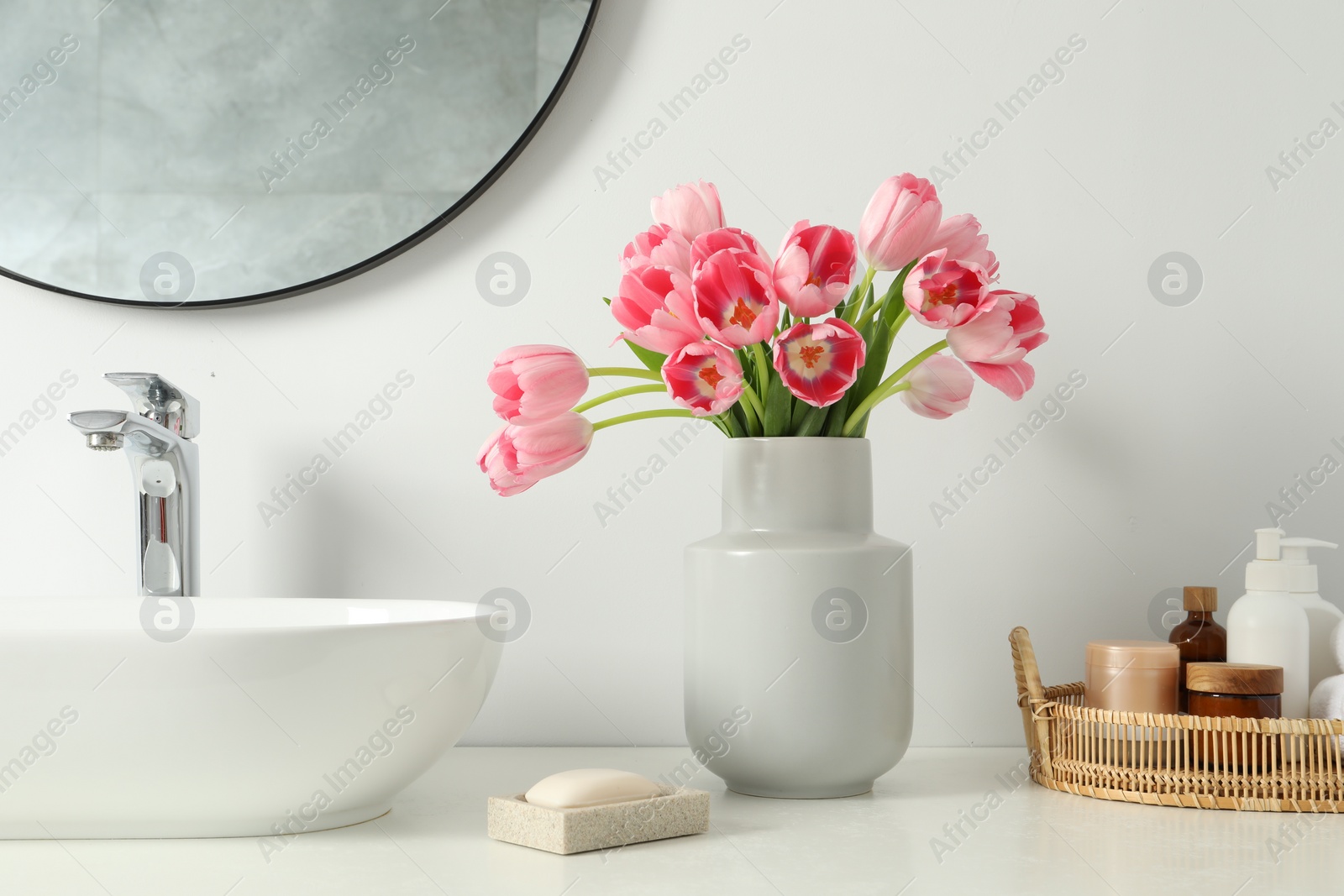 Photo of Vase with beautiful pink tulips and toiletries near sink in bathroom