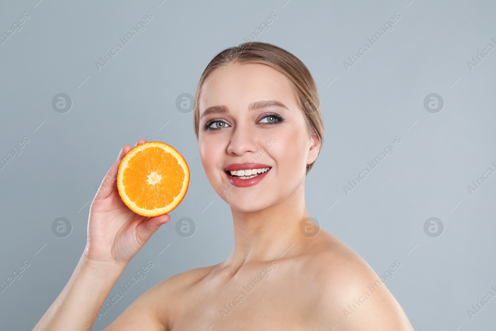 Photo of Young woman with cut orange on grey background. Vitamin rich food