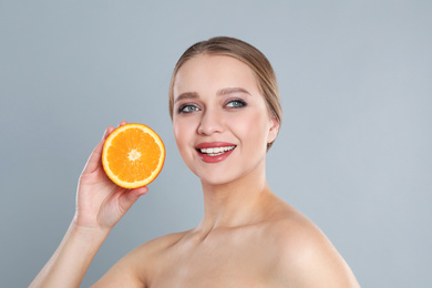 Young woman with cut orange on grey background. Vitamin rich food