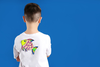Photo of Preteen boy with paper fish on back against blue background, space for text. April fool's day