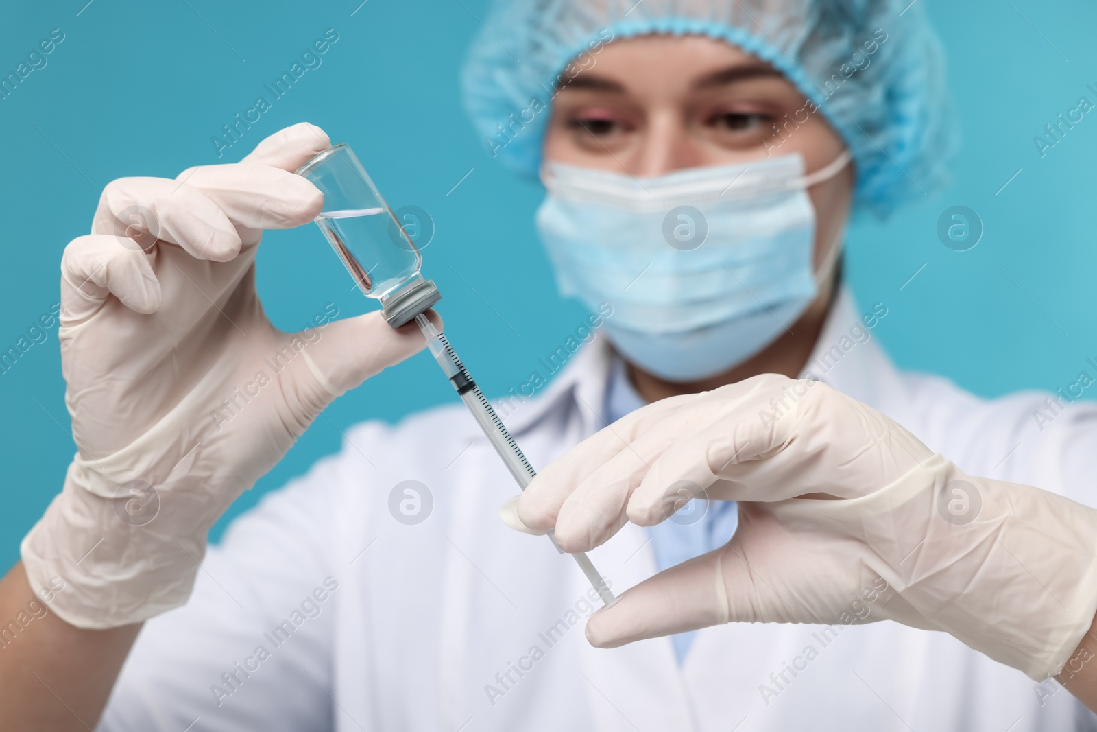 Photo of Doctor filling syringe with medication from glass vial on light blue background, selective focus