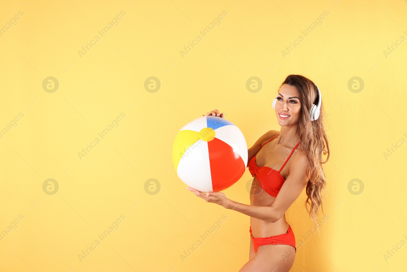 Photo of Pretty sexy woman in stylish bikini with headphones and beach ball on color background, space for text