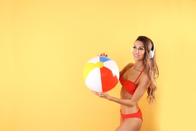 Pretty sexy woman in stylish bikini with headphones and beach ball on color background, space for text