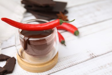 Photo of Glass of hot chocolate with chili pepper on white wooden table, closeup. Space for text