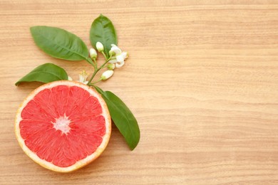 Photo of Cut fresh ripe grapefruit and green leaves on wooden table, flat lay. Space for text