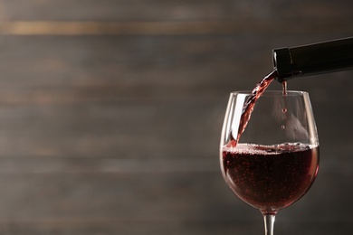 Pouring red wine into glass from bottle against blurred wooden background, closeup. Space for text