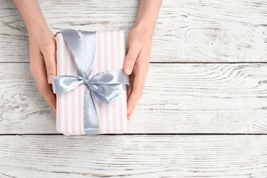 Photo of Young woman holding beautiful gift box on wooden background, top view