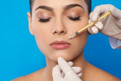 Photo of Young woman getting lips injection on color background, closeup. Cosmetic surgery