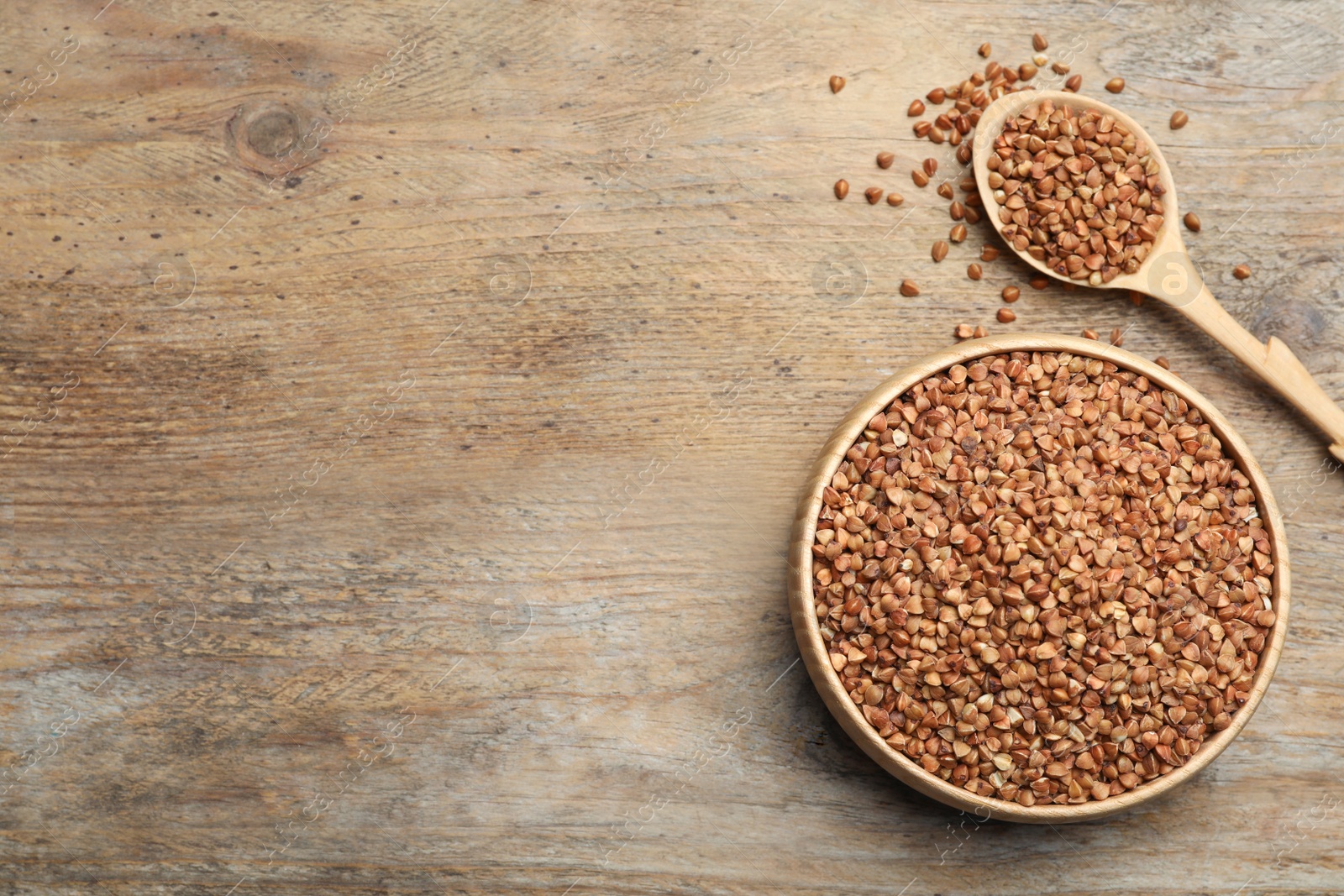 Photo of Bowl and spoon of uncooked buckwheat on wooden table, flat lay. Space for text