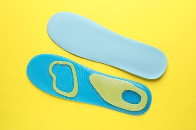 Photo of LIght blue orthopedic insoles on yellow background, flat lay